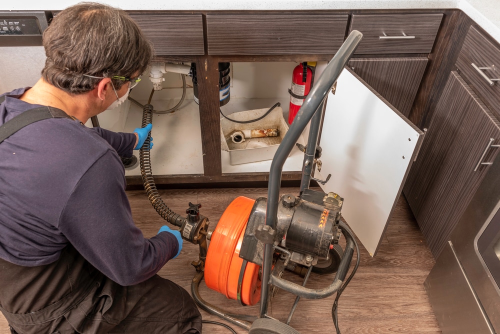 Professional,Plumber,Using,An,Auger,To,Clear,A,Kitchen,Sink